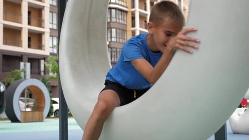 A Boy Rotates on a Round Plastic Swing Around Himself in the Yard Complex