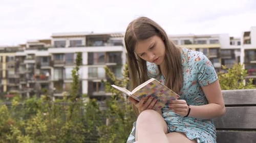 A Beautiful Young Caucasian Woman Reads a Book As She Sits on a Bench in an Urban Area