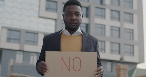 Slow Motion Portrait of Serious African American Man Holding NO Banner Standing Outdoors in City