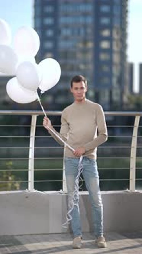 Man Smiling Holding White Balloons in Urban Setting