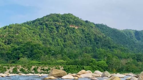 Low-angle view of a rocky mountain stream with gentle rapids and lush green hills in the