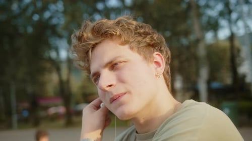 Young cool blond hair boy sitting in the park in fresh air, wearing headphones