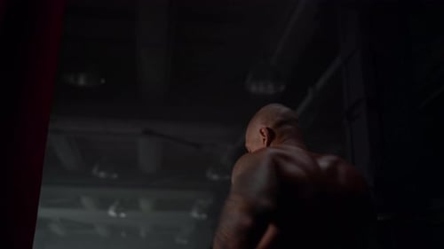 Muscular Man Punching Heavy Bag in Dark Gym