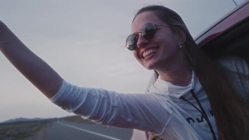 Beautiful Woman Leaning Out of Car Window and Waving Her Hand Out While Riding Through Countryside