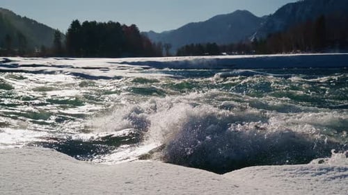 A Beautiful Flowing River Water Surrounded By Choppy Waves and Snowy Banks in a Stunning Mountainous