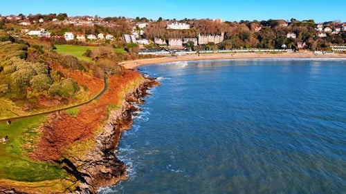 Bright sunlight illuminates a coastal scene with a mixture of cliffs, beach, and buildings.
