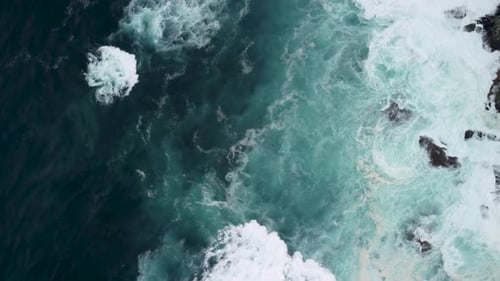Drone Rotating Over Powerful Waves Crashing On Rocky Coastline With Foamy Surfaces. Aerial Shot