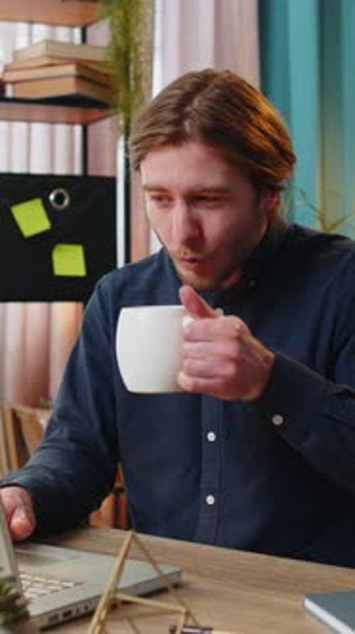Geschäftsmann, der am Laptop arbeitet und eine Tasse warmen heißen Kaffee trinkt, sitzt am Tisch, am Arbeitsplatz, zu Hause, im Büro
