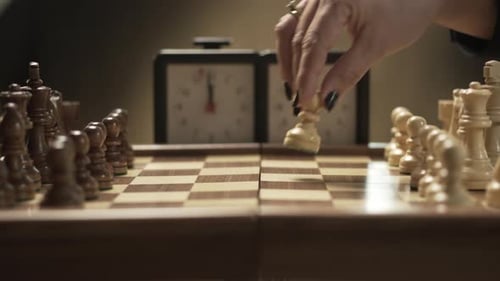 Chess game opening, pawn E2 to E4, female hand picks up chess piece and triggers chess clock