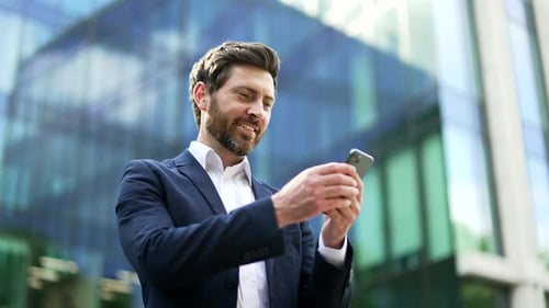 Handsome Man Uses Smartphone Outside Office Building