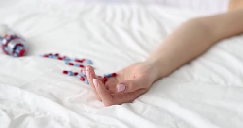 Woman's Hand with Pills on Bed