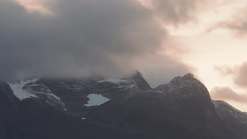 Des nuages orageux rétroéclairés par le soleil couchant passent au-dessus des sommets enneigés.