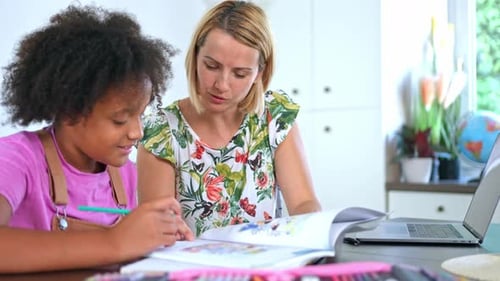Caucasian mother helping her beloved mixed race daughter with school homework at a desk
