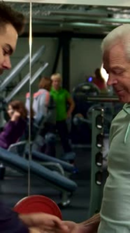Trainer Hands Barbell to Senior Client in Gym