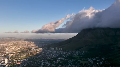 Thick dark clouds moving over dark Table mountain toward Cape Town in sunset