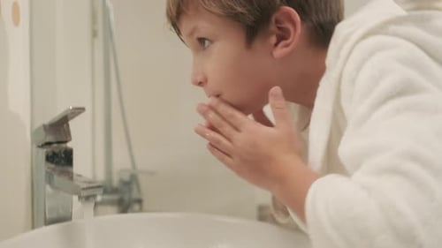 Niño pequeño que usa el lavabo del baño para lavarse la cara