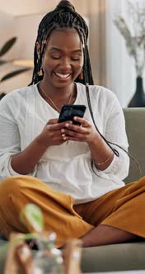 Woman Laughing While Using Smartphone on Couch
