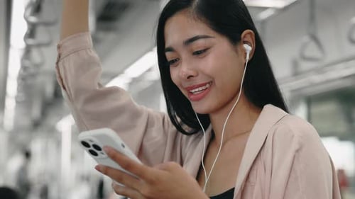 Woman Holding Onto Handrail in Subway Exploring Social Networks and Tuning Into Music on Mobile