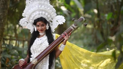 Beautiful Indian girl posing as Hindu Goddess Saraswati in woods and playing music with veena, slow