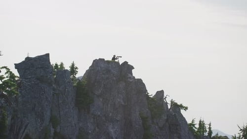 Photographer kneels on mountain ridge as silhouette against hazy sky, Tim Durkan wide tracking helic