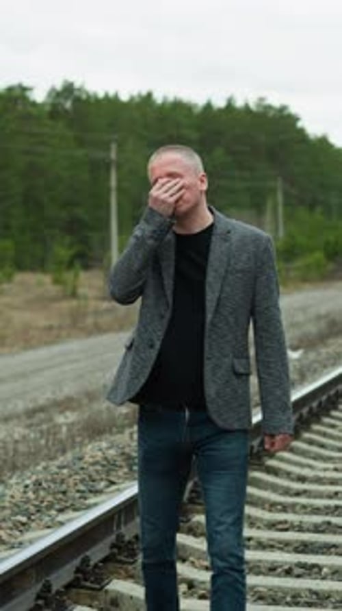 Pensive Man in Grey Suit Walking Along Railway Tracks in Forest