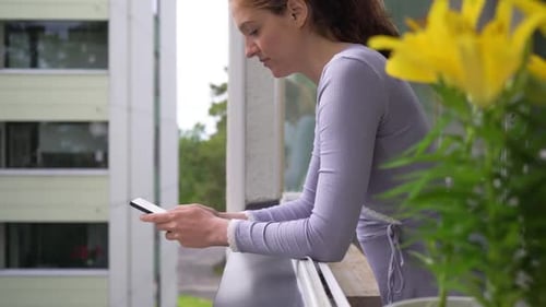 Woman Texts on Balcony with Yellow Lilies