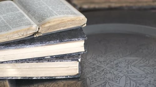Close-up tilt of old used books on decorated metal tray on table