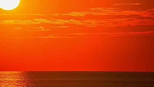 Time lapse shot of red fired sky during sunset behind tranquil ocean water in the evening