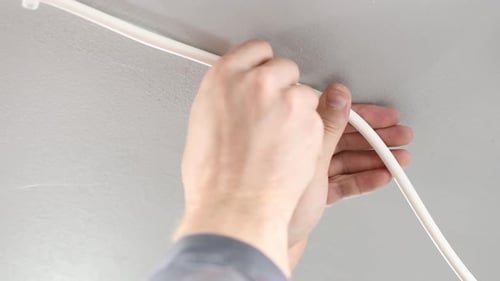 Profissional eletricista pregando o cabo elétrico no telhado com um martelo. Macho branco, cabo branco e chicote