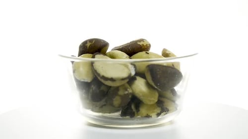Transparent glass bowl with Brazil nuts rotating on a white background. Flat plane. Eye level