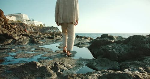 Person walking barefoot on volcanic rocks near ocean at sunset