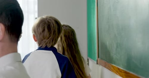Young multicultural boy and girl student write lesson drawing on chalkboard while male adult