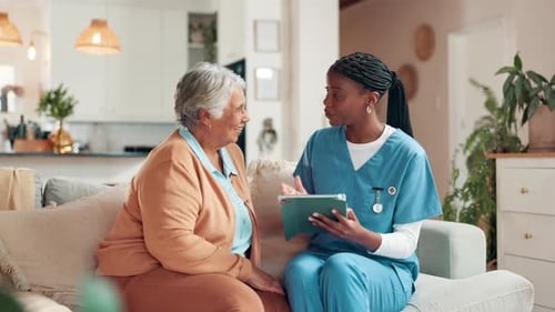Female Doctor Showing Tablet to Senior Woman at Home