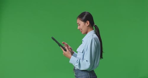 Side View Of Asian Business Woman Using Tablet On Green Screen Background In The Studio