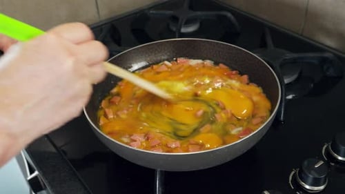 A close-up view of a freshly made omelette with ham being mixed in a frying pan on the stove in the
