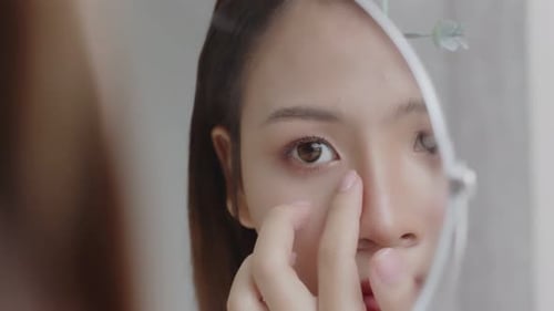 Close up reflection of young Asian woman applying concealer on face.