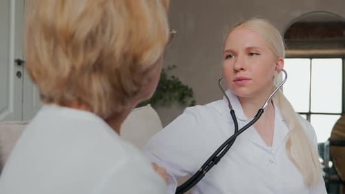 a Young Female Doctor Uses a Stethoscope to Listen to the Heart of a Pensioner