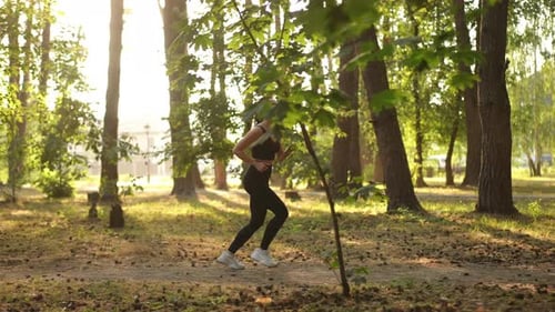 A Woman Running Energetically on a Beautiful Sunlit Forest Trail Surrounded By Nature