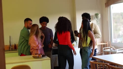 Group of multiracial friends with raised arms gathered in a kitchen while serving alcoholic beers to