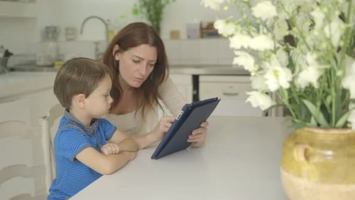 Mother and Child Interact with Tablet at Kitchen Table