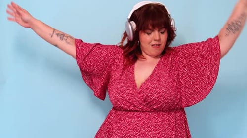 Plus-size woman dancing with headphones on blue background