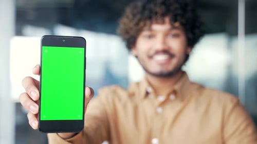 Close up of smartphone with green screen showing young businessman sitting in modern office. Color