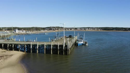 The camera flies past an elevated fishing pier that has a fishing boat docked up against it. The tid