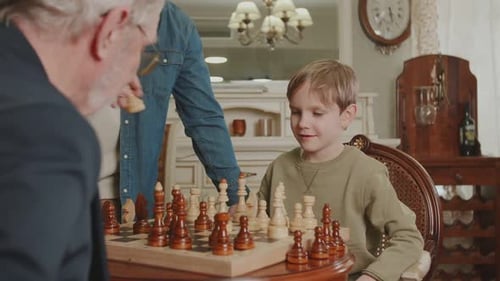 The child rearranges the chess piece on the chessboard. Dad is happy for his son, who, playing chess