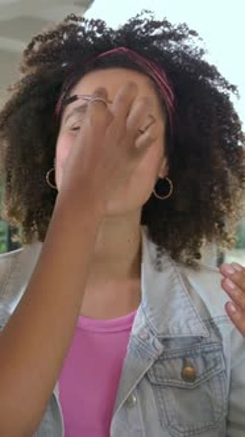 Vertical video: Reaching, artist hand blending product at counter for demo with brushes, pink top