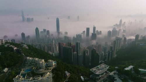 Wide shot of low coastal morning fog over the skyline of Hong Kong. Drone orbiting shot