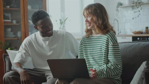 Couple Smiling and Using Laptop on Couch at Home