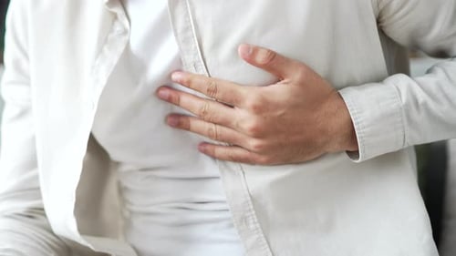 Close up. Male hands holding massaging chest. Young adult man in white shirt has heart attack while