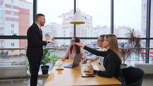 Processing and discussing graphs at meeting. Office team sit at the table sharing ideas.