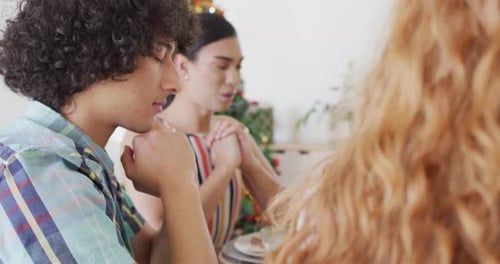 Happy group of diverse friends sitting at table and eating dinner, praying together